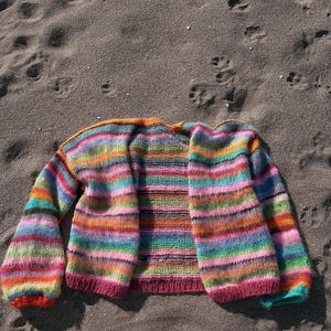 May include: A colorful striped cardigan with long sleeves and a loose fit. The cardigan is made of a soft, fuzzy yarn and has a relaxed, casual style.