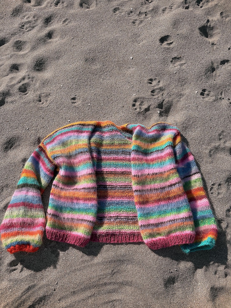 May include: A colorful striped cardigan with long sleeves and a loose fit. The cardigan is made of a soft, fuzzy yarn and has a relaxed, casual style.