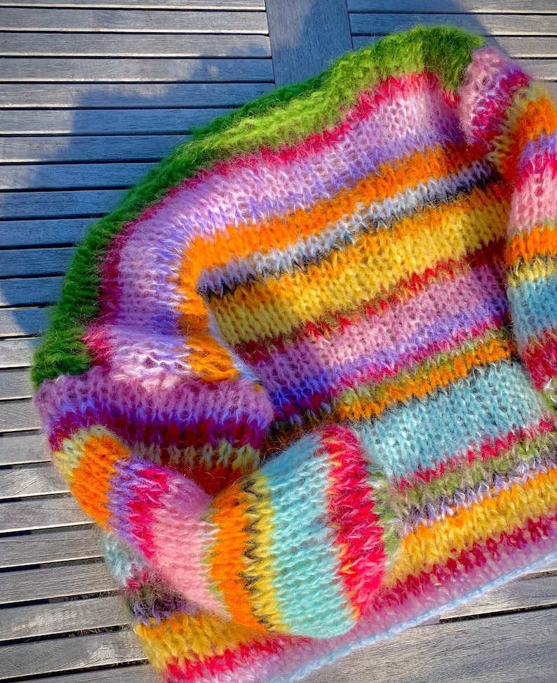 Puede incluir: Un su&eacute;ter de punto de rayas de colores con una textura peluda. El su&eacute;ter est&aacute; hecho con una variedad de colores, incluyendo rosa, verde, amarillo, naranja y azul.