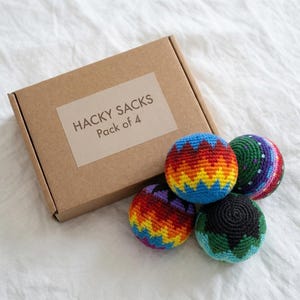 May include: A set of four colorful hacky sacks with a brown cardboard box. The hacky sacks are in various colors, including red, orange, yellow, blue, green, and purple. The box has a label that reads "HACKY SACKS Pack of 4".