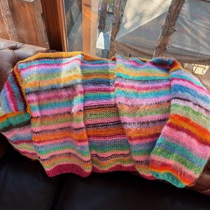 May include: A colorful striped cardigan with a loose fit and long sleeves. The cardigan is made of a soft, fuzzy yarn and has a relaxed, casual style.