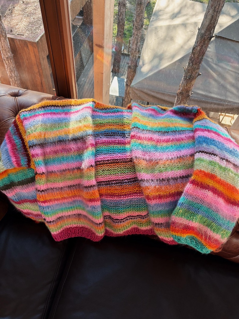 May include: A colorful striped cardigan with a loose fit and long sleeves. The cardigan is made of a soft, fuzzy yarn and has a relaxed, casual style.