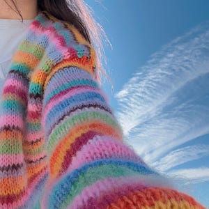 May include: A colorful striped cardigan with a fuzzy texture. The cardigan is made of a soft, knit fabric and features a variety of bright colors, including pink, blue, green, yellow, and orange.