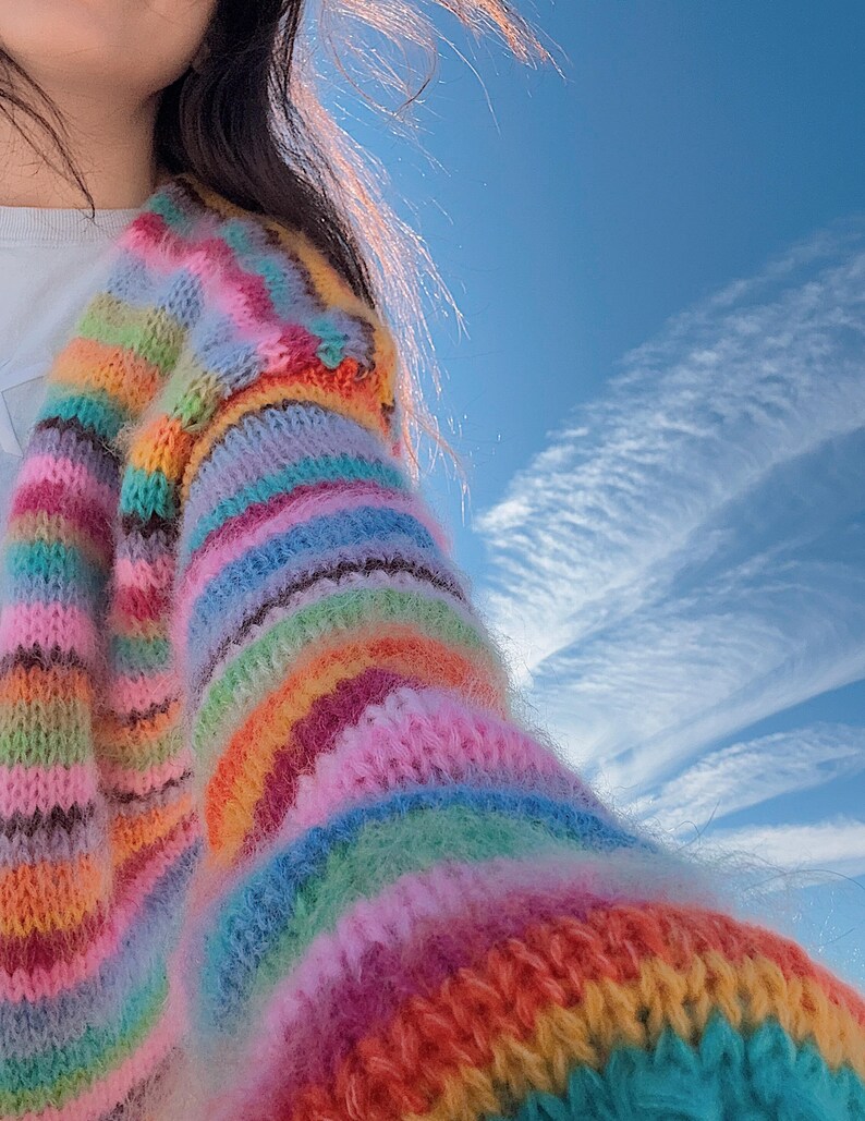 May include: A colorful striped cardigan with a fuzzy texture. The cardigan is made of a soft, knit fabric and features a variety of bright colors, including pink, blue, green, yellow, and orange.