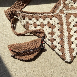 Puede incluir: Bolso de crochet hecho a mano en colores marr&oacute;n y crema. El bolso presenta un dise&ntilde;o de granny square y un estuche para gafas a juego, tambi&eacute;n de crochet. La correa tambi&eacute;n est&aacute; tejida. El estuche para gafas est&aacute; sujeto al bolso con un anillo met&aacute;lico.