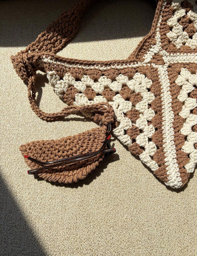 Puede incluir: Bolso de crochet hecho a mano en colores marr&oacute;n y crema. El bolso presenta un dise&ntilde;o de granny square y un estuche para gafas a juego, tambi&eacute;n de crochet. La correa tambi&eacute;n est&aacute; tejida. El estuche para gafas est&aacute; sujeto al bolso con un anillo met&aacute;lico.