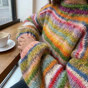 May include: A colorful, striped sweater with a round neckline. The sweater features a vibrant array of colors, including pink, orange, yellow, green, and blue. The sleeves are long and the material appears to be a soft knit.