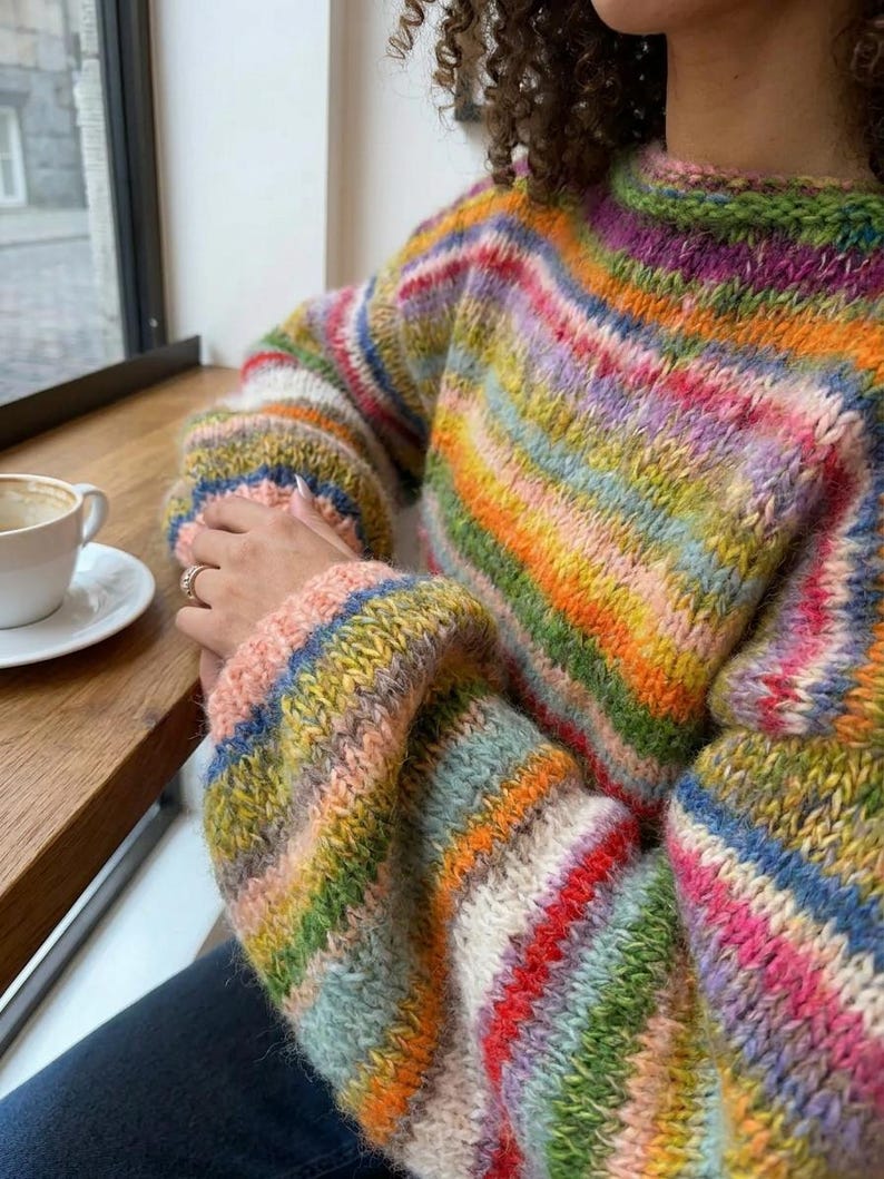 May include: A colorful, striped sweater with a round neckline. The sweater features a vibrant array of colors, including pink, orange, yellow, green, and blue. The sleeves are long and the material appears to be a soft knit.
