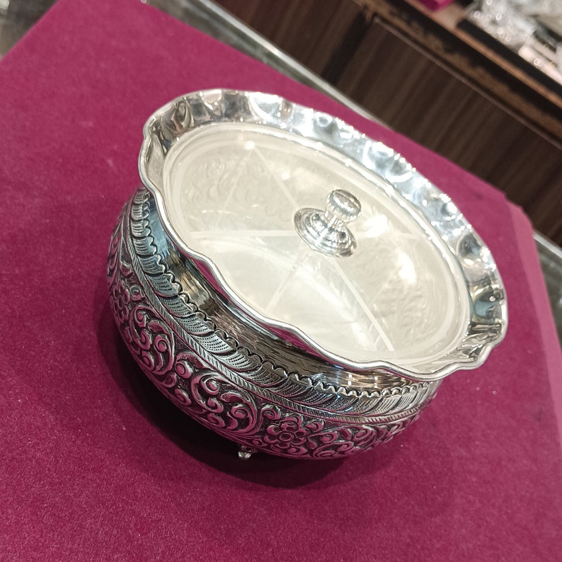 May include: A silver serving dish with a lid and four compartments. The dish is decorated with intricate floral patterns and has a scalloped edge.