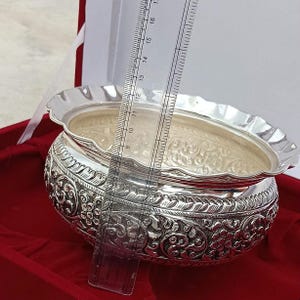 May include: A silver bowl with intricate floral designs, measuring approximately 11 inches in diameter. The bowl is displayed on a red velvet surface.