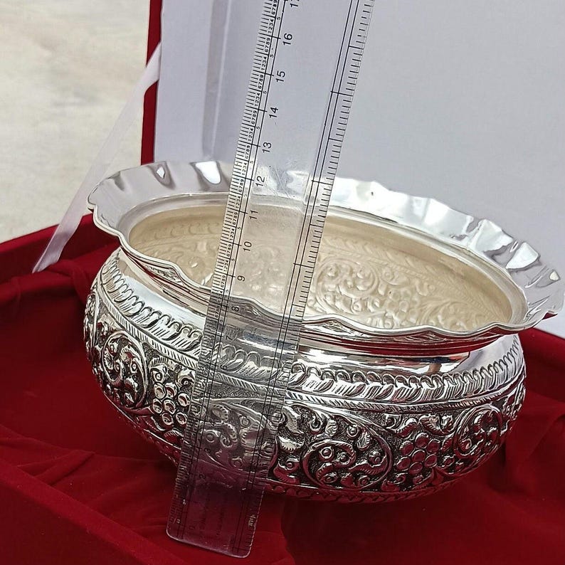 May include: A silver bowl with intricate floral designs, measuring approximately 11 inches in diameter. The bowl is displayed on a red velvet surface.