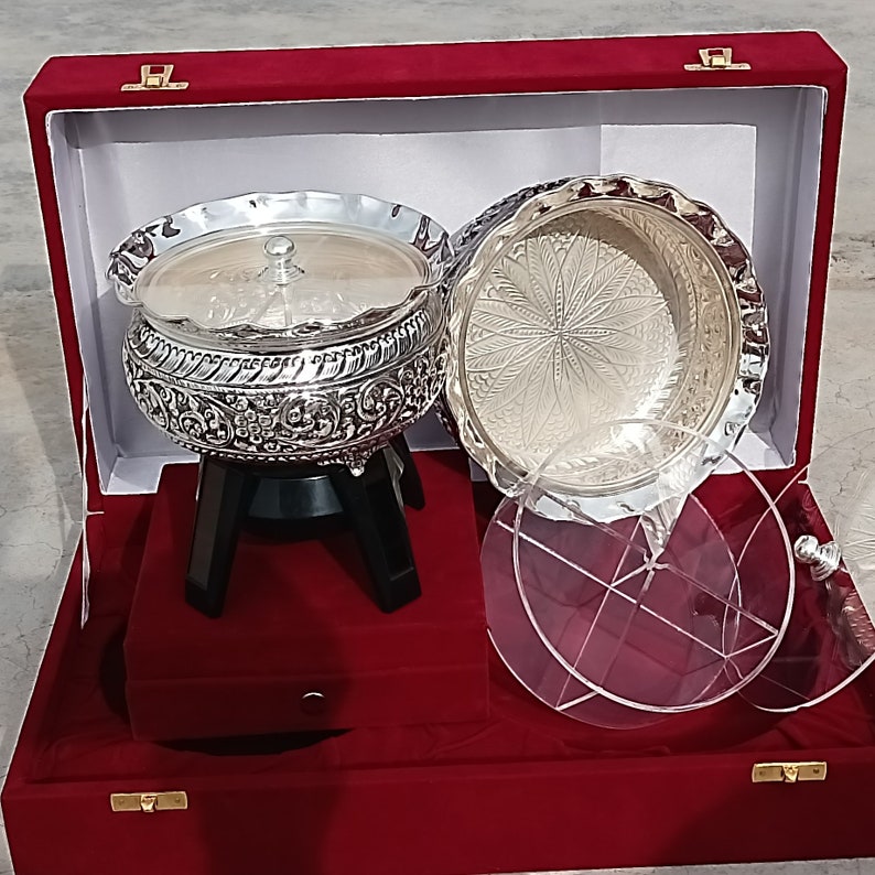 May include: A silver serving set with intricate designs, featuring a lidded bowl on a stand and a separate bowl. The set is displayed in a red velvet box with a clear acrylic lid.