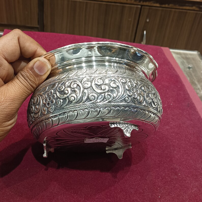 May include: A silver bowl with intricate floral designs and three legs. The bowl has a smooth, polished finish and is decorated with a raised floral pattern.