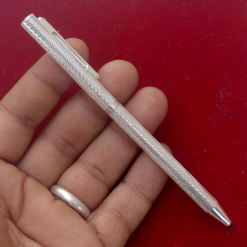 Puede incluir: Un bol&iacute;grafo de color plateado con un patr&oacute;n texturizado de l&iacute;neas entrecruzadas en todo el cuerpo cil&iacute;ndrico y la tapa. El bol&iacute;grafo incluye un clip de bolsillo delgado y recto unido a la tapa y una punta c&oacute;nica lisa en el extremo.