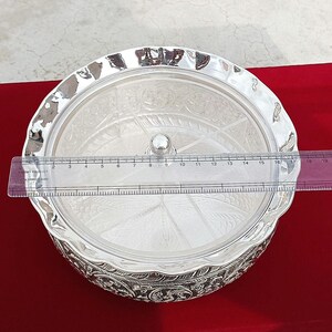 May include: A silver serving bowl with a lid and intricate designs. The bowl has a round shape and is divided into sections. The lid is clear and has a knob on top. The bowl is 18 inches in diameter.