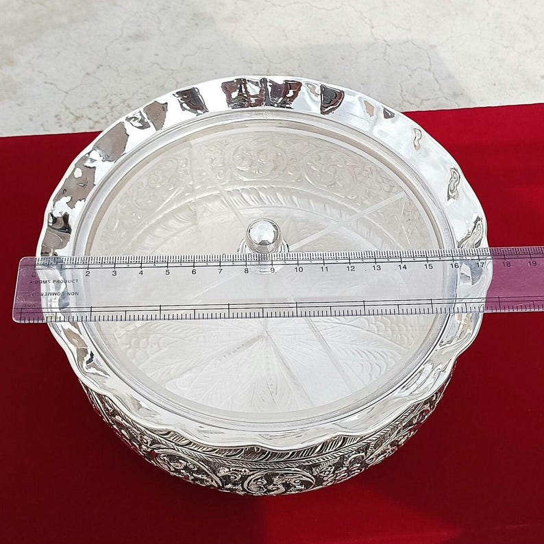 May include: A silver serving bowl with a lid and intricate designs. The bowl has a round shape and is divided into sections. The lid is clear and has a knob on top. The bowl is 18 inches in diameter.