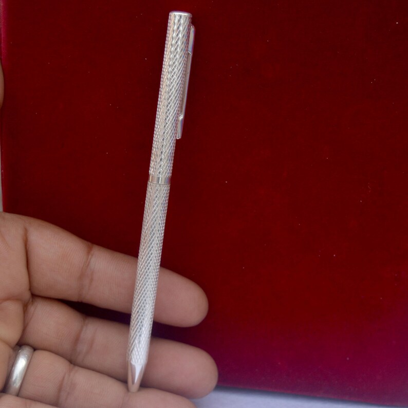 Puede incluir: Un bol&iacute;grafo de metal en tono plateado con un patr&oacute;n texturizado de l&iacute;neas entrecruzadas en el cuerpo y la tapa. El bol&iacute;grafo incluye un clip de bolsillo delgado e integrado en la parte superior y una punta c&oacute;nica lisa en el extremo.