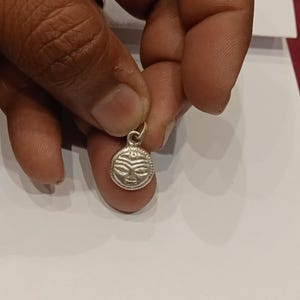 May include: Silver pendant with a circular design featuring a stylized face with a third eye.