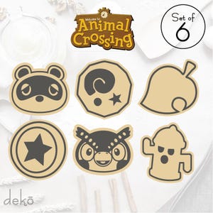 May include: Set of six Animal Crossing themed wooden cutouts. The cutouts feature characters and symbols from the popular video game series. The cutouts are beige and feature black and gray details. The cutouts include a raccoon, a leaf, a star, an owl, a fire hydrant, and a spiral.