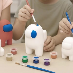 May include: White Among Us figurines being painted with blue paint. The figurines are surrounded by small paint pots in various colors, and paintbrushes. The figurines are red, white, and unpainted. A fun, creative activity for all ages.