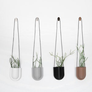 Op de afbeelding: Vier hangende plantenbakken met planten erin. De plantenbakken zijn wit, grijs, zwart en bruin. De planten zijn allemaal van hetzelfde type en zijn groen.