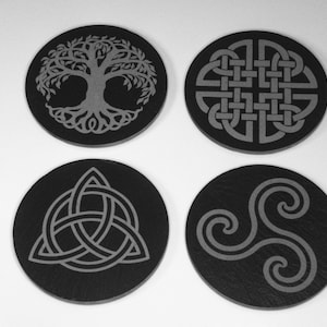 May include: Four black slate coasters with different Celtic designs. The designs include a tree of life, a trinity knot, a Celtic knot, and a triskelion.