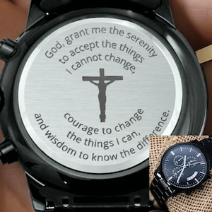 May include: Black wristwatch with a stainless steel back featuring an engraved cross and the text "God, grant me the serenity to accept the things I cannot change, courage to change the things I can, and wisdom to know the difference."