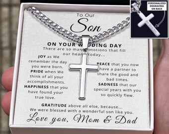 May include: A silver cross pendant necklace presented in a gift box. The cross is centered on a silver chain. The box contains a message to a son on his wedding day, with text that reads "Love you, Mom & Dad."