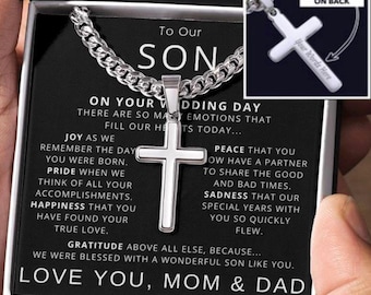 May include: A silver cross necklace in a black gift box with a message to a son on his wedding day. The message reads "On your wedding day there are so many emotions that fill our hearts today... Joy as we remember the day you were born. Pride when we think of all your accomplishments. Happiness that you have found your true love. Gratitude above all else, because... we were blessed with a wonderful son like you. Love you, Mom & Dad".