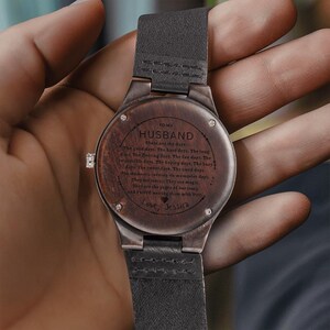 Pode incluir: Um rel&oacute;gio de pulso de madeira com uma pulseira de couro escuro. O mostrador do rel&oacute;gio &eacute; gravado com as palavras "TO MY HUSBAND" e uma mensagem personalizada. O rel&oacute;gio tem um acabamento em madeira castanha escura.