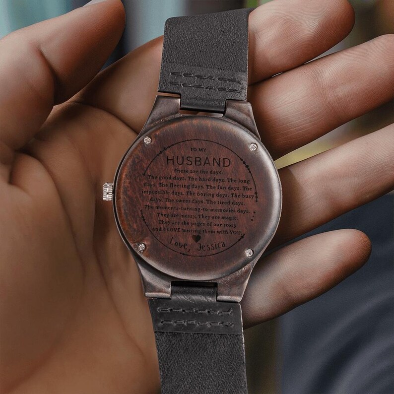 Pode incluir: Um rel&oacute;gio de pulso de madeira com uma pulseira de couro escuro. O mostrador do rel&oacute;gio &eacute; gravado com as palavras "TO MY HUSBAND" e uma mensagem personalizada. O rel&oacute;gio tem um acabamento em madeira castanha escura.