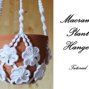 Pode incluir: Um suporte de planta de macramé branco com um vaso de terracota. O suporte é feito com um padrão de nós que se assemelha a flores. O texto "Macrame Plant Hanger Tutorial" está escrito em itálico em um fundo branco.