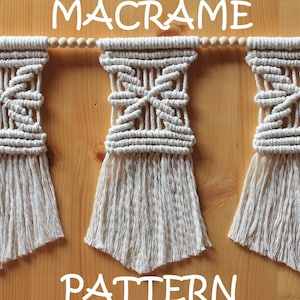 May include: A macrame wall hanging pattern with three white macrame pieces with wooden beads strung between them. The macrame pieces have a fringe at the bottom and a geometric pattern in the center. The text "MACRAME PATTERN" is written in white letters on a wooden background.