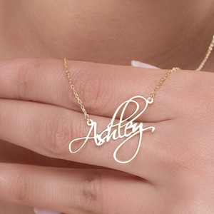 May include: Gold necklace with a cursive script nameplate that reads "Ashley".