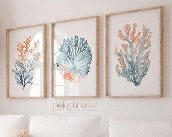 May include: Three framed watercolor prints of coral in shades of blue, orange, and pink. The prints are hung on a white wall above a white couch with pillows and a throw blanket.