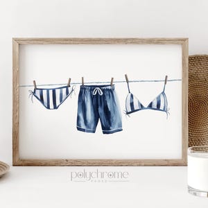 May include: A watercolor illustration of blue and white striped swimwear hanging on a clothesline. The swimwear includes a bikini top, swim bottoms, and a pair of swim trunks. The illustration is framed and has the text "polychrome" printed below the image.