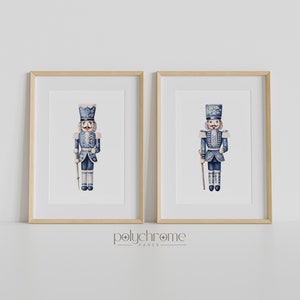 May include: Two framed prints of blue and white watercolor illustrations of nutcracker soldiers. Each print features a nutcracker soldier with a blue and white uniform, a white hat, and a white staff.