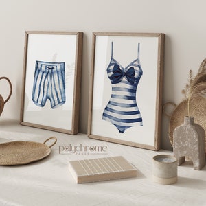 Pode incluir: Duas impress&otilde;es emolduradas de ilustra&ccedil;&otilde;es de aquarela de roupas de banho listradas. A impress&atilde;o &agrave; esquerda mostra uma sunga listrada azul e branca. A impress&atilde;o &agrave; direita mostra um mai&ocirc; listrado azul e branco com um la&ccedil;o azul.