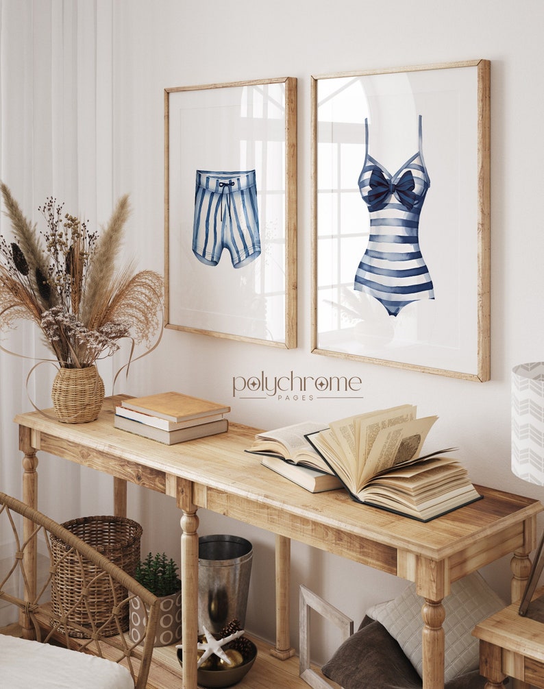 May include: Two framed watercolor illustrations of striped swimwear. The left illustration shows blue and white striped swim trunks. The right illustration shows a blue and white striped swimsuit with a bow. The frames are natural wood and the illustrations are on white paper. The text "polychrome pages" is printed below the illustrations.