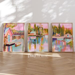 May include: Three framed paintings of a lake scene with a pink sky, green trees, and a small cabin on the water. The paintings are in a modern style with abstract brushstrokes.