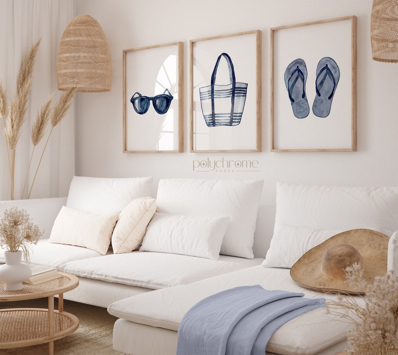 May include: Three framed watercolor illustrations of summer essentials: sunglasses, a striped tote bag, and flip flops. The illustrations are in shades of blue and white and are set against a white background. The frames are natural wood.