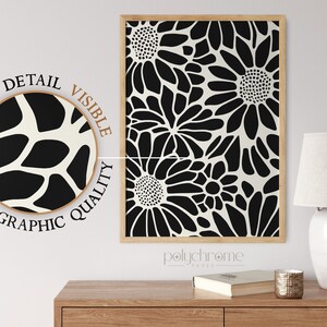 May include: A black and white floral print art print with a wood frame. The print is of stylized flowers with a white background. The print is labeled "polychrome pages".