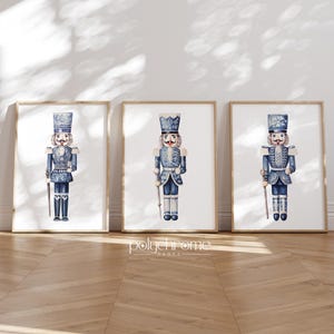 May include: Three printable art prints featuring blue and white watercolor illustrations of nutcracker soldiers. Each print features a different nutcracker soldier with a unique design.