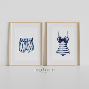 Pode incluir: Duas impress&otilde;es emolduradas de ilustra&ccedil;&otilde;es de aquarela de roupas de banho listradas. A impress&atilde;o &agrave; esquerda mostra uma sunga listrada azul e branca. A impress&atilde;o &agrave; direita mostra um mai&ocirc; listrado azul e branco com um la&ccedil;o.