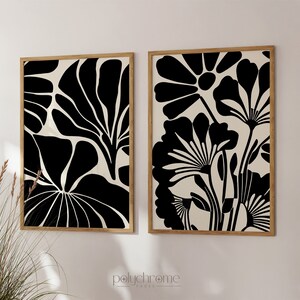 May include: Two black and white abstract floral prints in wooden frames. The prints feature stylized flowers and leaves.