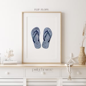 May include: A watercolor painting of a pair of blue flip flops with black straps. The painting is framed and displayed on a shelf with other beach-themed decor.