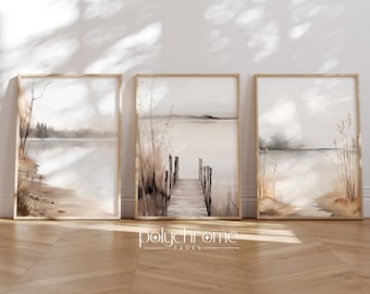 Puede incluir: Tres pinturas de acuarela enmarcadas que representan una escena de lago con un muelle de madera que se extiende hacia el agua. Las pinturas están en tonos de marrón, beige y gris, con una sensación suave y de ensueño. Las pinturas están colgadas en una pared blanca con un suelo de madera.