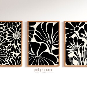 May include: Three framed black and white floral prints with a cream background. The prints are arranged in a row on a white wall.
