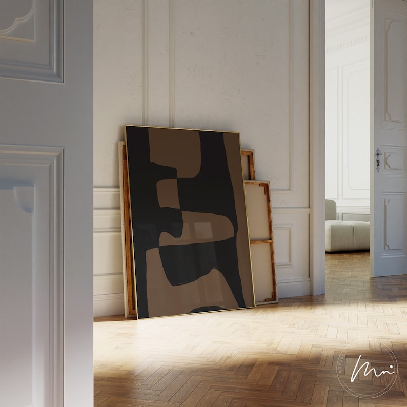 May include: A framed abstract art print with brown and black geometric shapes. The print is leaning against a white wall.