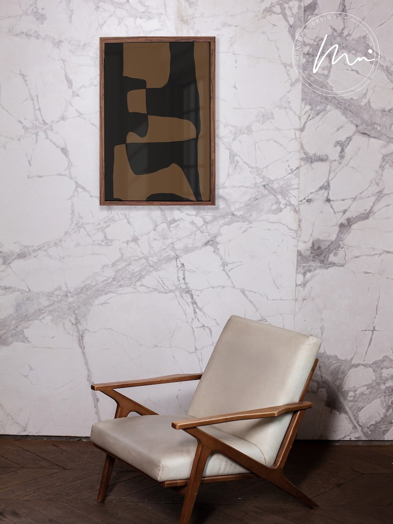 May include: A framed abstract art print with brown and black geometric shapes against a white marble wall. A white armchair with wooden arms sits in front of the wall.
